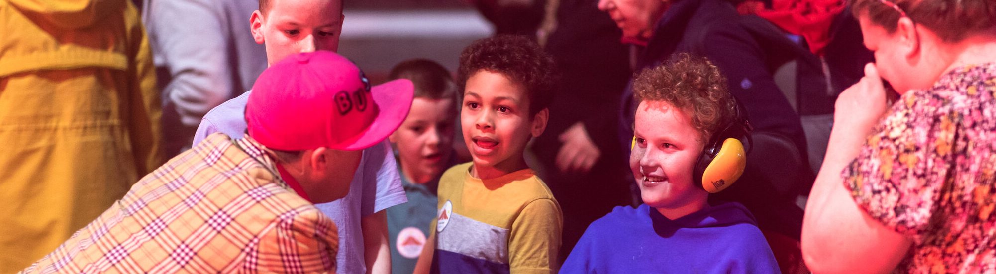 A little boy wearing ear defenders smiles at the circus clown.