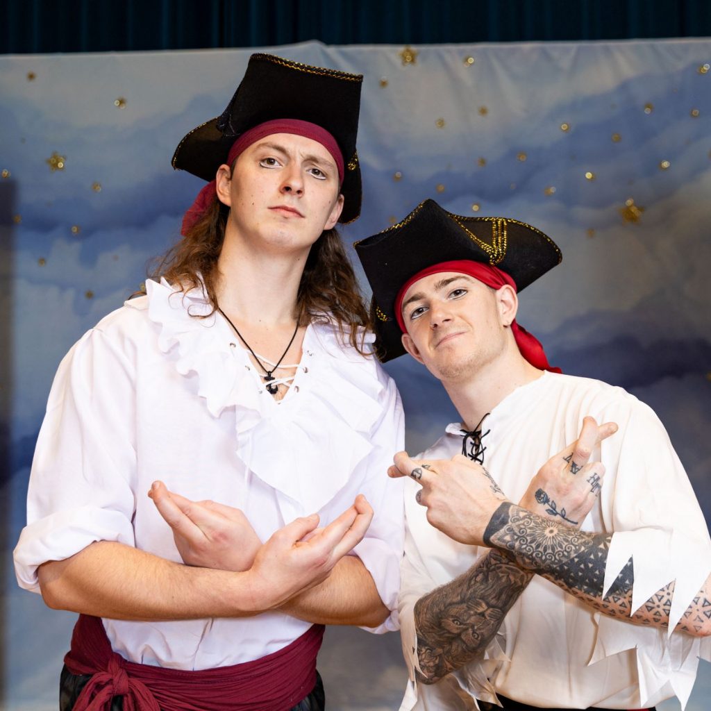 Two acrobats are wearing pirate outfits and crossing their fingers.