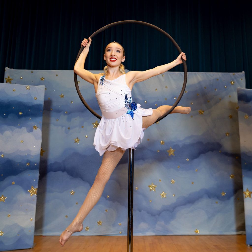 A woman is stretching whilst balancing on a hoop that is held high on a stick. 