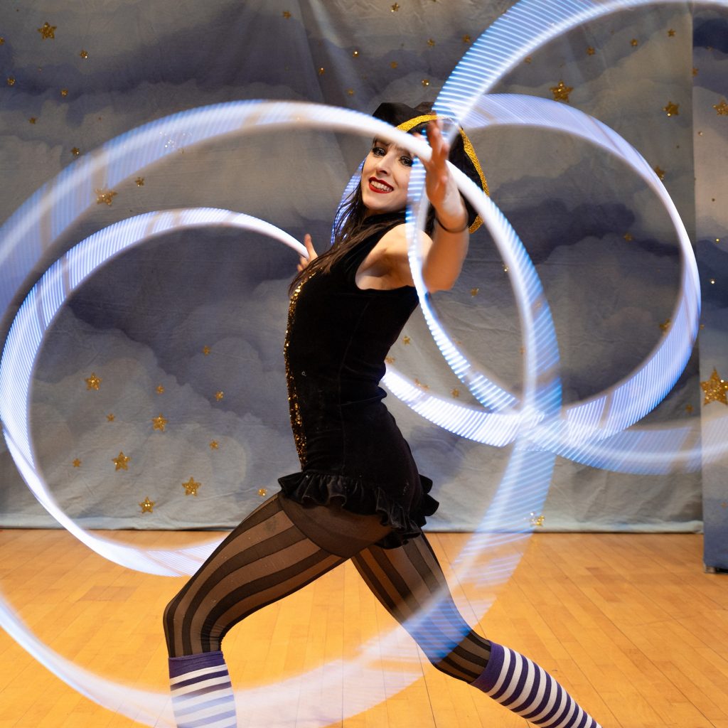 A woman is twirling light up hula hoops. 