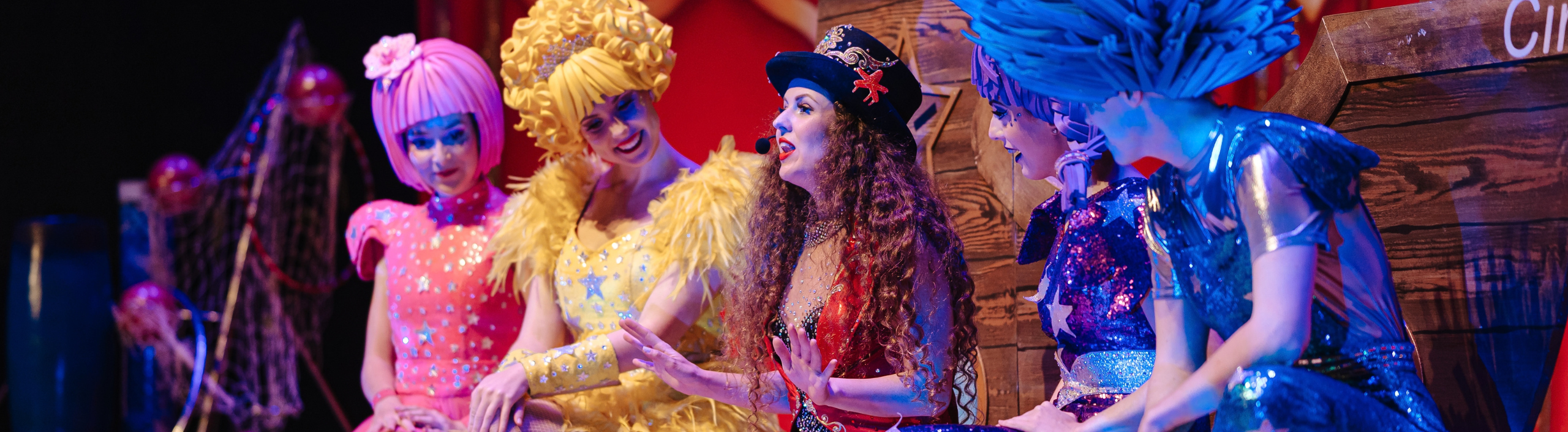 A group of performers are on stage, they are wearing sparkly colourful clothing.