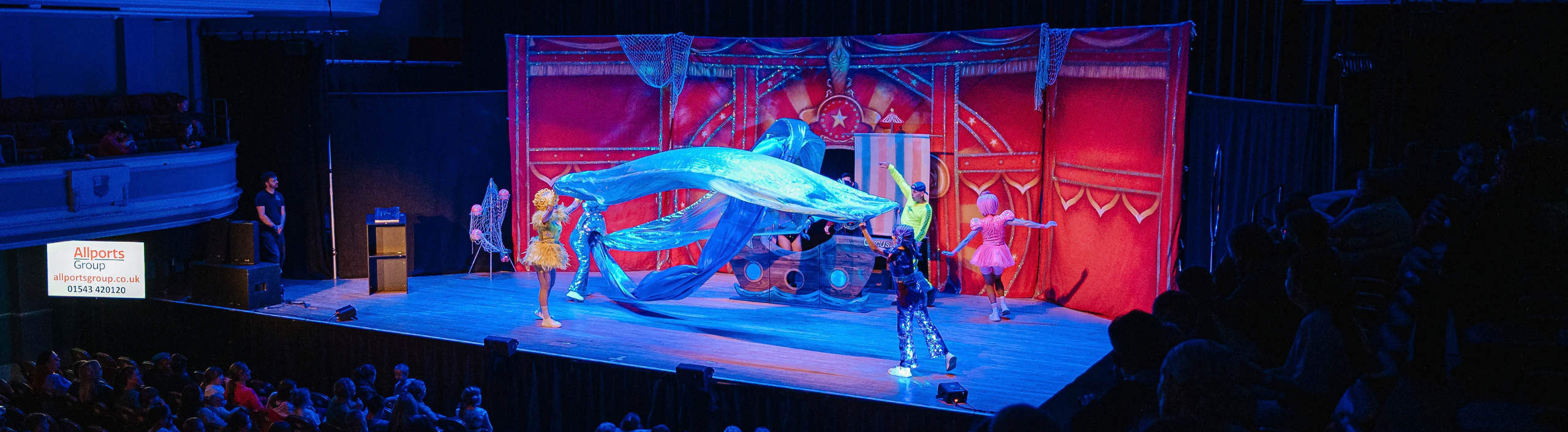 The Circus Starr troupe are on stage, they are moving pieces of material on stage to represent waves or the sea.