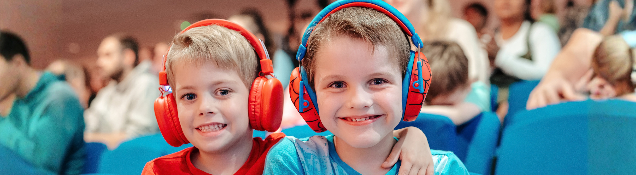 Two little boys are smiling at the camera. One boy has his arm wrapped around the others shoulder. Both are wearing ear defenders.