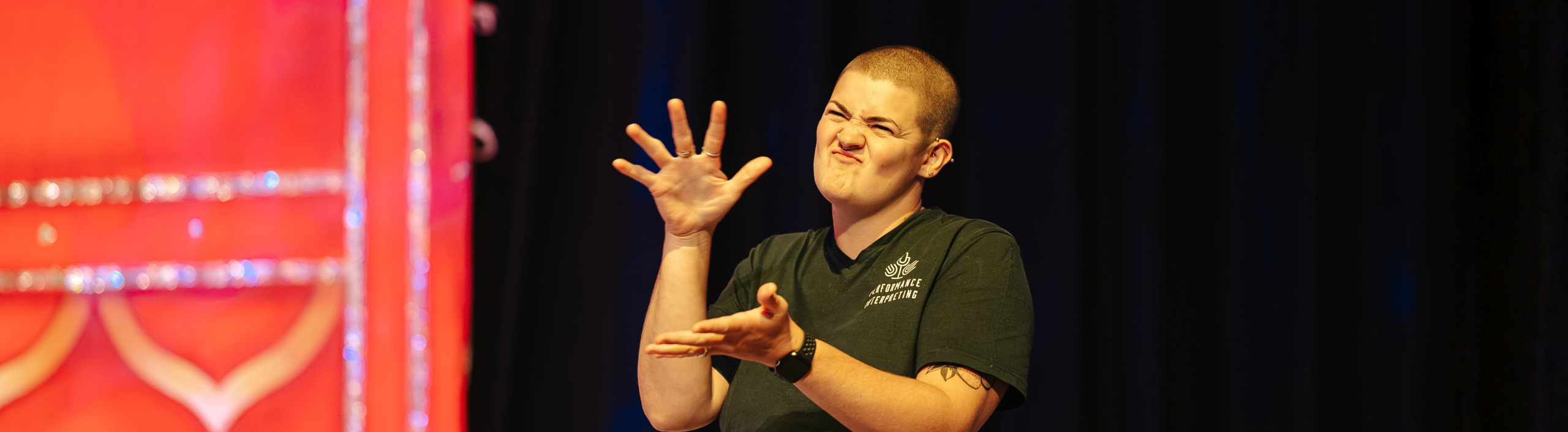 A woman is interpretating at the side of the stage, she is moving her hands as she signs in British Sign Language.